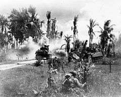 U.S. troops advancing towards a palm jungle, behind tanks on Panay Island.