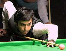A photograph of a man playing Snooker wearing white shirt and black waistcoat.