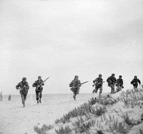 Men in extended line advance over a desert landscape