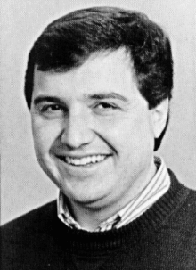 Black and white portrait photograph of smiling man in his forties wearing short and sweater.