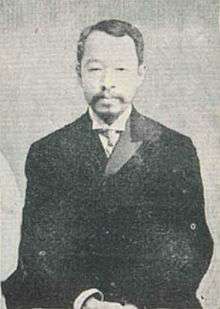 A monochrome photograph of a bearded Korean man in a suit