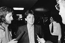 Paul McCartney being interviewed by two reporters holding microphones.