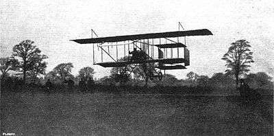 monochrome photograph of a biplane flying low over a field