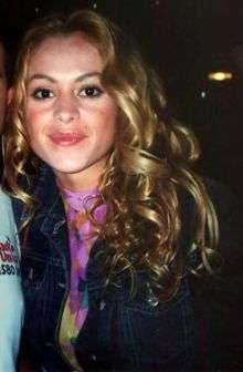A young woman wearing a blouse with flower and has curly blonde hair.