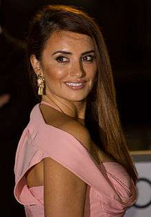 A close-up image of a Hispanic female wearing a pink dress and a pair of gold earrings with pink opals.