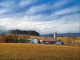 A grouping of farm buildings backdropped by a field, mountains, and the sky.