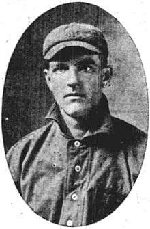 A man wearing a dark baseball jersey with a high collar and a cap.