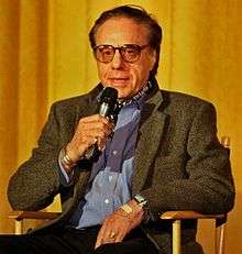 Bogdanovich seated at a director's chair with a microphone in his hand