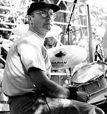 A black-and-white picture of a man sitting at a drum kit