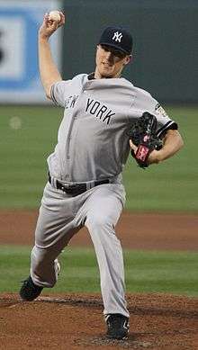 A man in a grey jersey, which says "New York" across the front, throws a baseball.