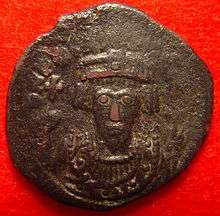 A copper coin with the bust of Phocas. His eyes form the central focus of the image