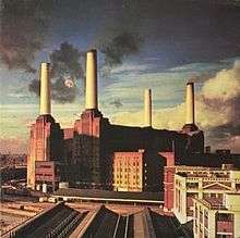 An image of the Battersea Power Station in England, where a giant pig can be seen flying between its left chimneys.