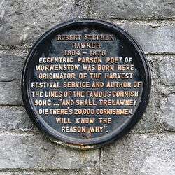 A black circular plaque with gold-coloured lettering. It reads: ROBERT STEPHEN HAWKER 1804 – 1875 ECCENTRIC PARSON POET OF MORWENSTOW WAS BORN HERE. ORIGINATOR OF THE HARVEST FESTIVAL SERVICE AND AUTHOR OF THE LINES OF THE FAMOUS CORNISH SONG ..."AND SHALL TRELAWNEY DIE THERE'S 20,000 CORNISHMEN WILL KNOW THE REASON WHY".