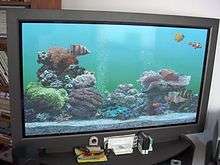 Photograph of a flat panel displaying an aquarium; the aquarium has several fish swimming around, a gravel bottom, and decorative rocks and plants.