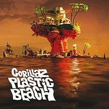 The cover of the third Gorillaz album "Plastic Beach". An artificial island rests on the ocean during a sunset. Apart from the base, it is mostly mushroom-shaped. It contains a few palm trees and small buildings. At the very top is a large white building with many windows. Other objects in and around the island include a ship, a buoy, a lighthouse and a crate. The view shows the opposite side of the island from the "Experience Edition" cover. In the lower left corner are the uppercase words "Gorillaz Plastic Beach" on separate rows. They are white and in a thick, wavy font.