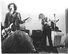 A black and white photo, with two band members playing.