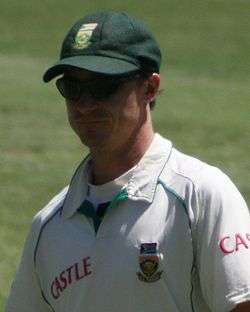 A man in South Africa Test cricket uniform, wearing a green cap and a pair of sunglasses, standing in the field