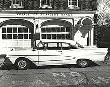 1960s white sedan parked in front of a brick building