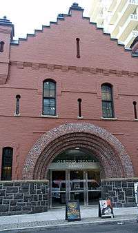 Two story brick building opening onto the sidewalk. Entrance is set in  rounded arches.