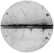 track of subatomic particle moving upward through cloud chamber and bending left (an electron would have turned right)
