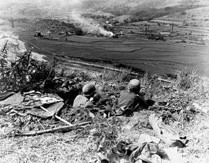 Men sit in foxholes watching over a lower terrain feature