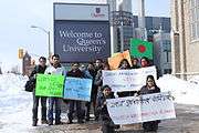 Students holding placards in front of "Queen's University" sign