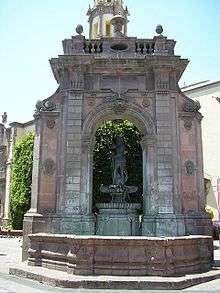 A fountain under an arch with a figure wielding a trident on top.