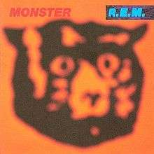 An album cover showing a blurred drawing of a cat's head in black against an orange background. The name of the album is in red text in the top-left corner of the cover and the band's name is in blue text on a black background in the top-right corner of the cover.