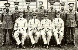 Portrait of eleven men in military uniforms with peaked caps, seven standing and four seated