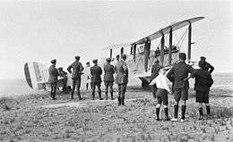 Military biplane parked at an airfield with a crowd of spectators