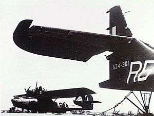 Black-painted military amphibious aircraft in background, with tail assembly of similar aircraft in right foreground