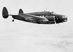 Twin-engined twin-tailed military monoplane in flight, side-on