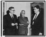 Three men standing and having a conversation. All three men are wearing suits.
