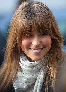 A smiling woman with long brown hair and a white scarf.