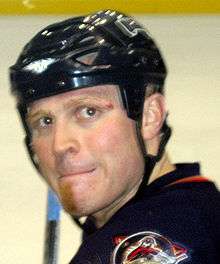 A close-up view of a Caucasian ice hockey player's face. He wears a black helmet and is looking to the right.