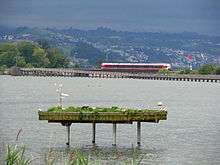 SOB Flirt of the S40 line crossing the Seedamm at Rapperswil; Holzbrücke Rapperswil-Hurden in the foreground.