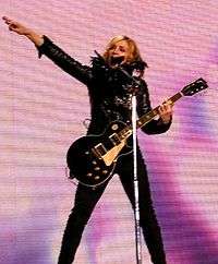 Woman wearing a black outfit while singing and playing a guitar.