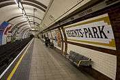 An underground railway platform with the words "Regent's Park" inlaid in tile in the right-hand wall and geometrical wall decoration visible further along the wall