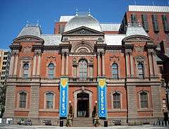 Photograph of the Renwick Gallery, an old brick building with colorful contemporary banners flanking the main entry and announcing "American Craft".