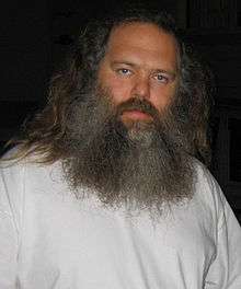 A man in a white shirt with long gray hair and a long beard