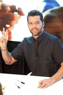 A man wearing a black shirt is showing the two-finger peace sign