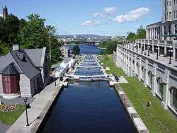 A small canal with a set of locks leading from a river near a large city.