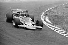 Black-and-white photograph of Rindt racing a flat and winged Formula One car through a corner