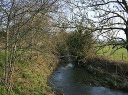 a narrow stretch of river, surrounded by trees on banks either side, sunny day, some clouds