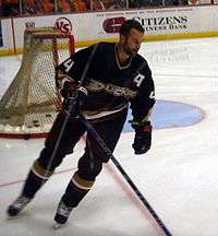 Hockey player in black Anaheim ducks uniform. He skates near the goal with his stick on the ice.