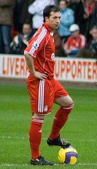 A man dressed all in red standing with his hands on his hips and his left foot on a yellow ball