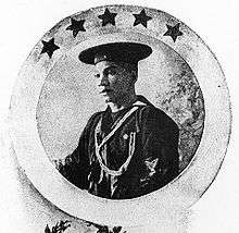 Head and torso of a young black man in sailor suit and flat cap with a lanyard around his neck. Around the portrait is a circular frame with five stars.