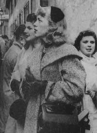 Picture of a woman standing in a crowded street, looking away from the camera