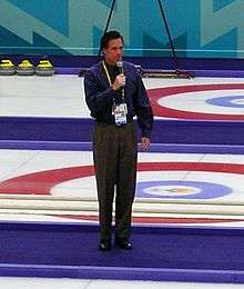 Photograph of Romney standing with microphone in middle of curling lanes