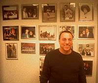 A middle-aged, bespecatacled man smiles in front of a wall covered with New York Cosmos memorabilia.
